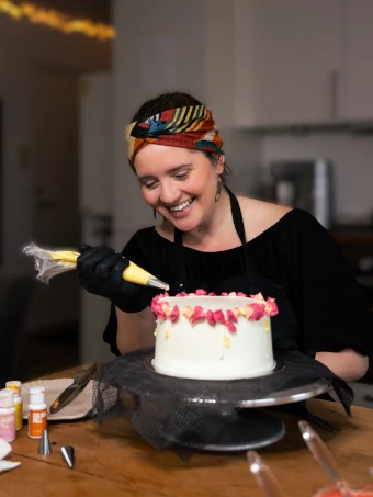 Cake decorator smiling while piping pink buttercream flowers onto a cake