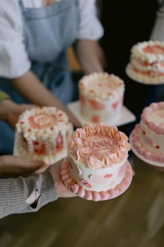 Hands holding decorated mini cakes during a Cake Atelier community gathering